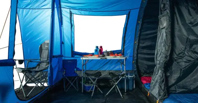 Wnętrze niebieskiego namiotu z rozstawionym stołem, krzesłami i śpiworami. Dobra wodoodporność namiotu zapewnia komfortowe warunki.