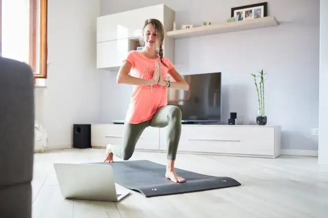 Kobieta ćwiczy jogę w domu, patrząc na laptopa.
