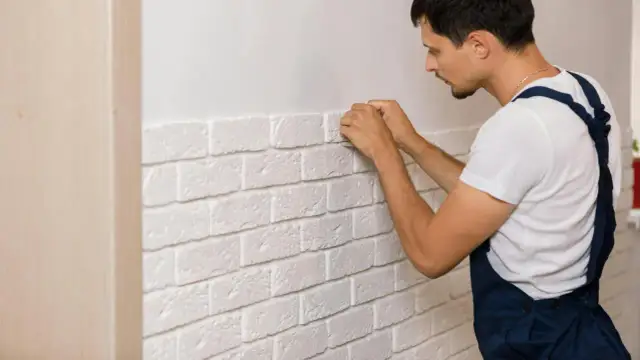 Mężczyzna montuje biały kamień dekoracyjny na ścianie. Odpowiedź na pytanie: czy kamień dekoracyjny można kłaść na farbę? Tak, można!