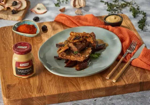 Żeberka w miodzie z dodatkami na talerzu, obok słoiczek musztardy i przyprawy.