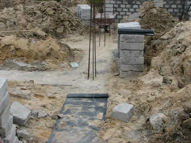 Budowa fundamentów: betonowe pustaki, zbrojenie, czarna folia izolacyjna i ziemia.