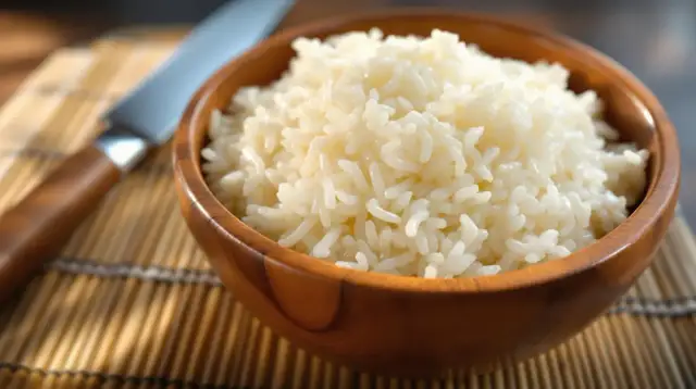 Miseczka idealnie ugotowanego ryżu do sushi na macie bambusowej, obok nóż.