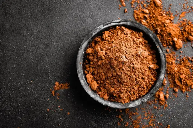 Miseczka z kakao na ciemnym tle, rozsypane kakao obok.