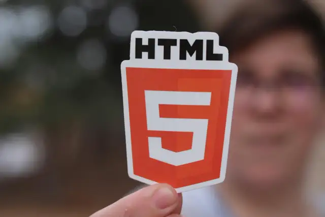 Osoba trzyma naklejkę z logo HTML5, symbolizującą wiedzę, jak utworzyć stronę html.