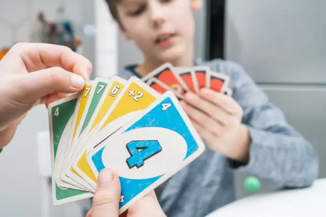 Dłonie trzymają karty do gry Uno. W tle widać chłopca grającego w Uno.