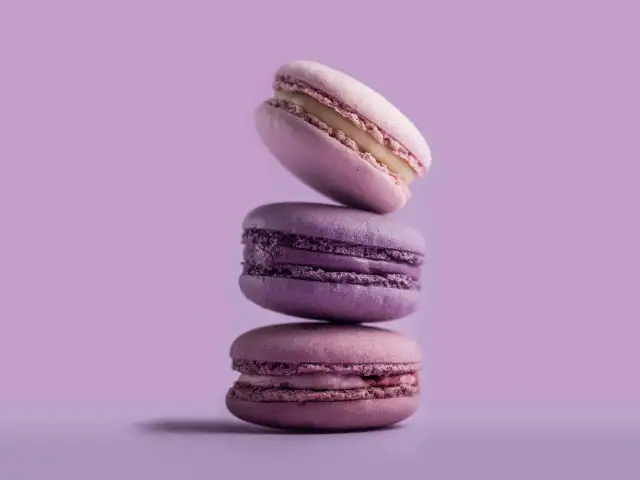 Stos trzech fioletowych makaroników na pastelowym tle.