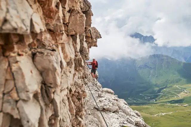 Wspinacz na via ferrata w Dolomitach, z widokiem na kręte drogi i zielone doliny.