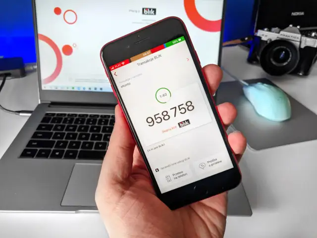 Dłoń trzyma smartfon z aplikacją Blik, na ekranie widoczny kod transakcji.