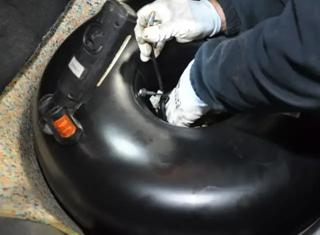 Ręce w rękawiczkach montują lub demontują okrągły zbiornik LPG w bagażniku samochodu.