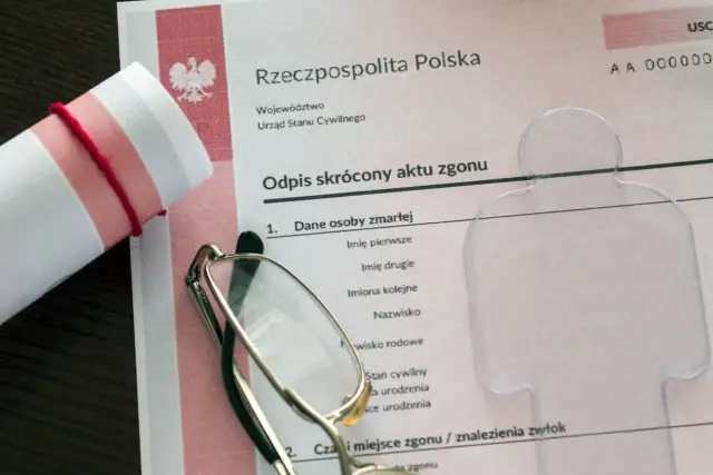 Odpis skrócony aktu zgonu z okularami i zrolowanym dokumentem.