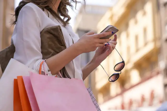 Kobieta z zakupami sprawdza telefon, planując refinansowanie pożyczki.