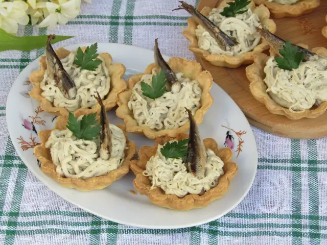 Wielkanocne przystawki: kruche babeczki z pastą rybną i śledzikiem, ozdobione natką pietruszki.