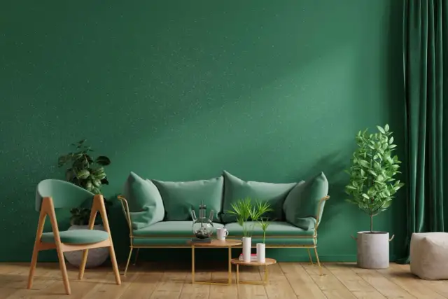 Zielona ściana z brokatem, sofa, krzesło i rośliny tworzą przytulne wnętrze. Dowiedz się, jak nałożyć brokat na ścianę, by uzyskać taki efekt.