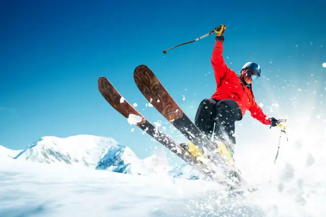 Narciarz w czerwonej kurtce zjeżdża po ośnieżonym stoku, unosząc śnieg.