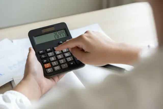 Dłoń naciska przycisk kalkulatora z widocznym wynikiem 264.75.