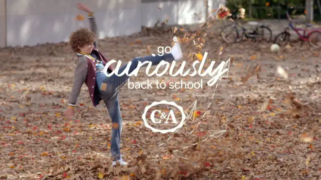 Chłopiec w jesiennych ubraniach kopie liście, z napisem "go curiously back to school" i logo C&A.