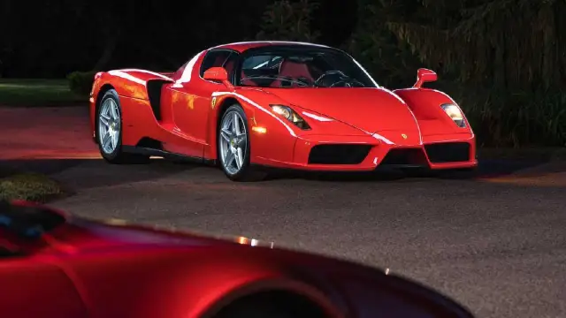 Czerwone Ferrari Enzo zaparkowane nocą na drodze, z innym czerwonym samochodem w tle.
