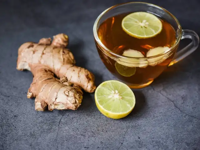 Imbir, plasterki cytryny i kubek herbaty imbirowej z cytryną.