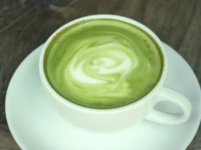 Zielony, spieniony napój w białej filiżance na spodku. To matcha latte, co to za napój?