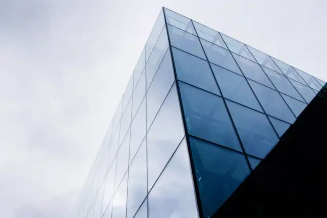 Nowoczesny budynek z geometrycznymi, błękitnymi szybami fotowoltaicznymi odbijającymi niebo.