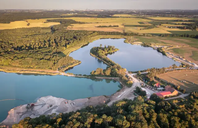 Widok z lotu ptaka na żwirownię z jeziorami, lasem i polami w tle.