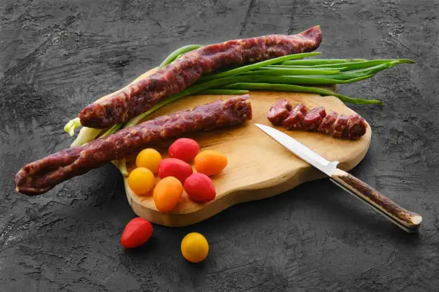 Dwa kabanosy, pomidorki i szczypiorek na desce. Czy koty mogą jeść kabanosy? Lepiej nie ryzykować.