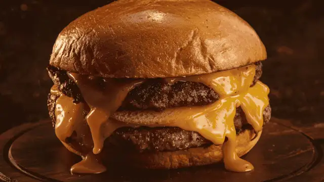 Gros plan sur un burger double au fromage fondant dégoulinant, sur un pain brioché doré.