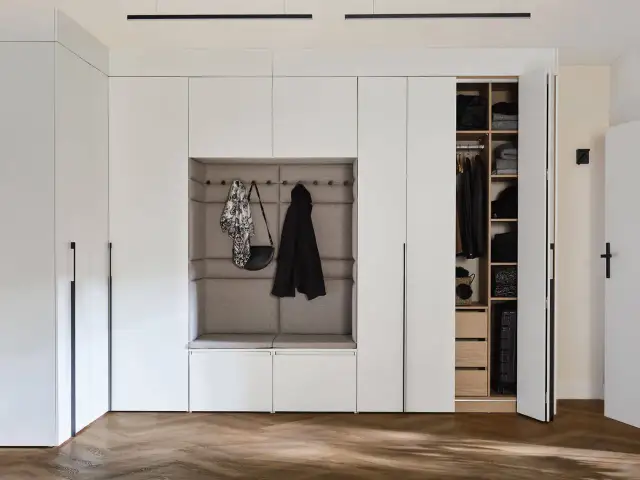 Nowoczesna zabudowa wnęki w przedpokoju z tapicerowanym siedziskiem i otwartą szafą.