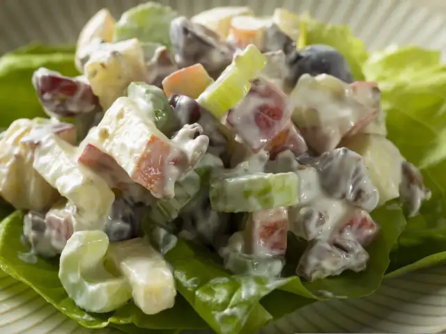 Pyszna sałatka z selera, jabłek, rodzynek i winogron, polana kremowym sosem. Idealna na lekki posiłek.