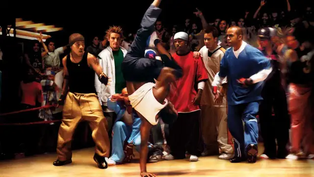 Tancerz wykonuje akrobację na parkiecie, otoczony przez widzów. Scena jak z najlepszych filmów o tańcu ulicznym.