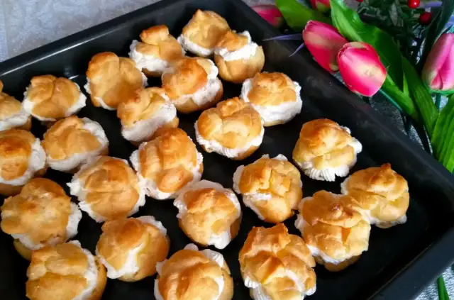 Ptysie przepis: złociste, puszyste ptysie wypełnione kremem, gotowe do podania. Obok bukiet różowych tulipanów.