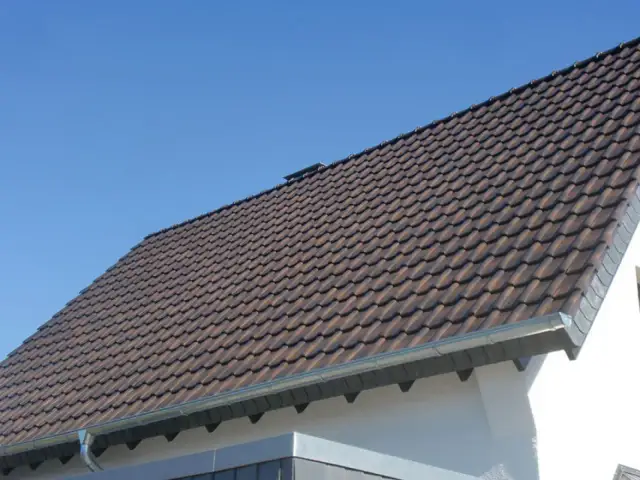 Dachówki ceramiczne na dachu domu, z widocznym okapem. Okap jest kluczowy, by wiedzieć, ile powinien wystawać dach poza ścianę, chroniąc ją przed deszczem.