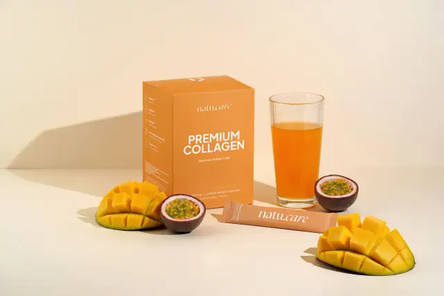 Pudełko z napisem "PREMIUM COLLAGEN Naturalny kolagen rybi", szklanka z pomarańczowym napojem, kawałki mango i marakui.