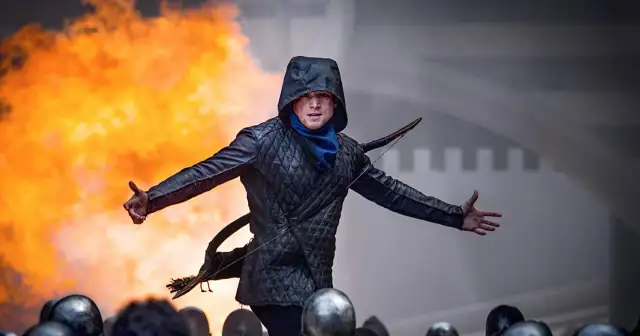 Robin z Sherwood w kapturze, z łukiem, na tle płomieni i zbrojnych.