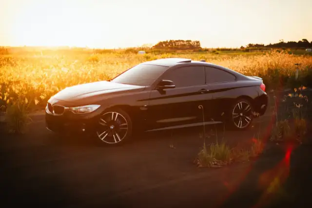 Czarny sportowy samochód na tle zachodzącego słońca i pól. Idealny moment na zakup, gdy vat na samochody jest korzystny.