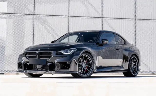 Czarny sportowy samochód z felgami i czerwonymi zaciskami hamulcowymi na tle nowoczesnej ściany.