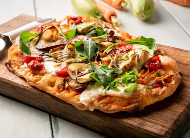 Chrupiący spód do pizzy z bakłażanem, cukinią i pomidorkami, posypany rukolą i mozzarellą.