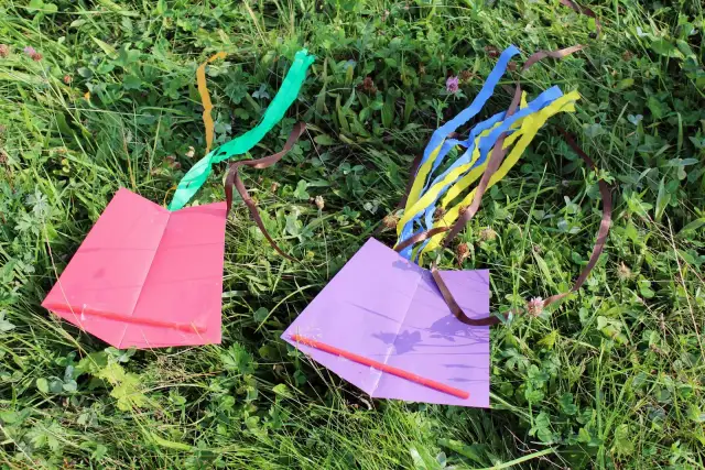Dwa proste latawce, różowy i fioletowy, leżą na trawie. Idealne, by pokazać jak zrobić latawiec.