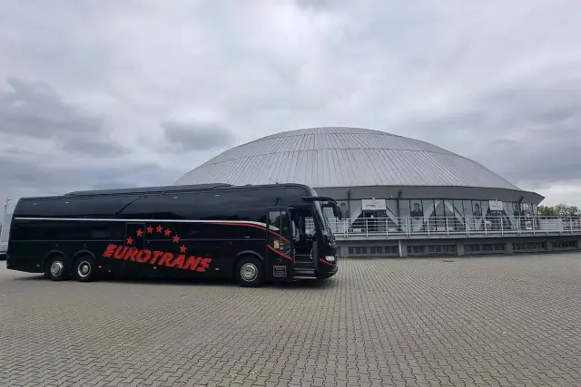 Czarny autokar turystyczny "Eurotrans" przed nowoczesnym budynkiem z kopułą.