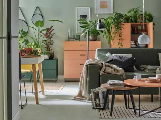 Salon z kanapą w kolorze zielonym i meblami w odcieniach pomarańczowego. Mnóstwo roślin tworzy przytulną atmosferę.