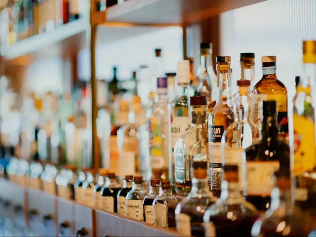 Rząd butelek z alkoholami, niektóre z etykietami wskazującymi, ile likier ma procent.
