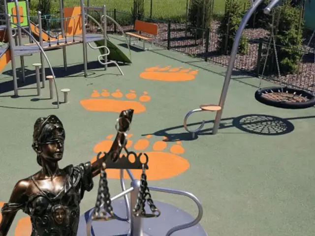 Figurka Temidy z wagą na placu zabaw z pomarańczowymi śladami stóp.