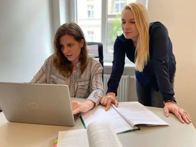 Dwie kobiety przy biurku analizują dokumenty i pracują na laptopie.