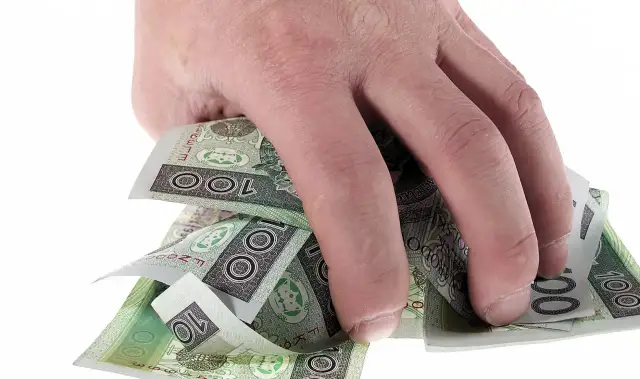 Dłoń trzyma plik polskich banknotów 100 zł. Może to symbolizować zwrot refinansowania lub po prostu oszczędności.