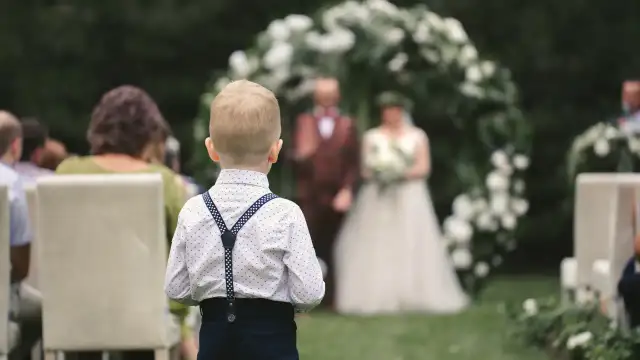 Chłopiec w białej koszuli z szelkami stoi tyłem do widza, na tle ślubu.