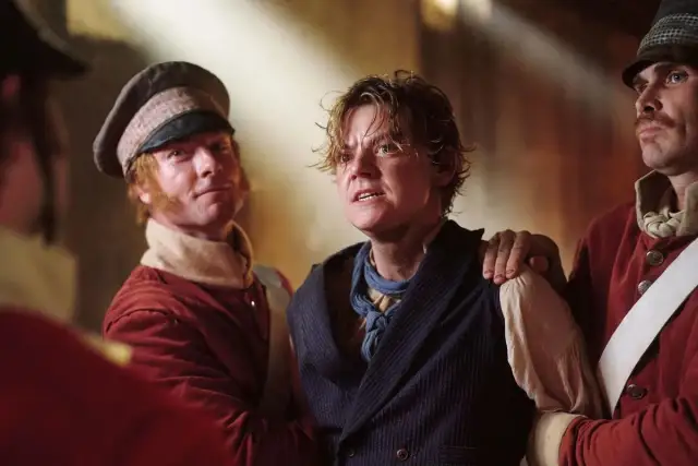 Młody mężczyzna, niczym **the artful dodger**, z wyrazem strachu na twarzy, jest trzymany przez dwóch mężczyzn w strojach z epoki.