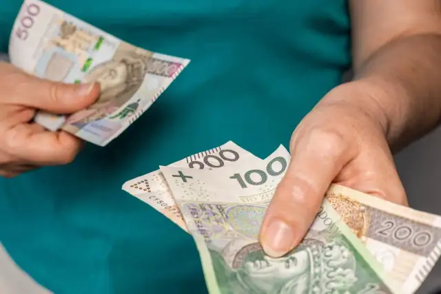 Dłonie trzymają polskie banknoty o nominałach 100, 200 i 500 zł.