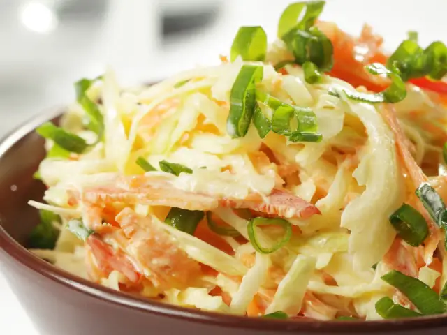 Surówka z białej kapusty i marchewki z zieloną cebulką w brązowej misce.