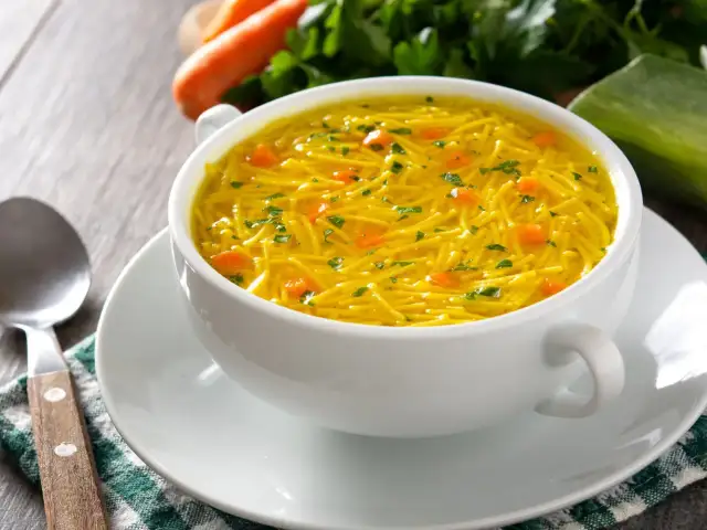 Biała miseczka z gorącym bulionem z makaronem nitki i kawałkami marchewki.