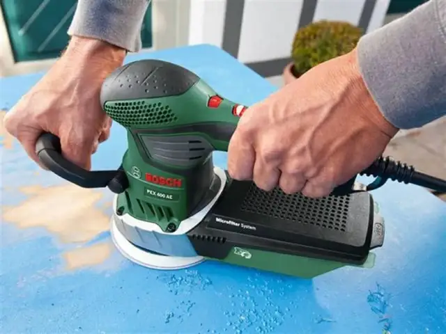 Ręce trzymają zieloną szlifierkę Bosch PEX 400 AE, która jest idealna do szlifowania gipsu.